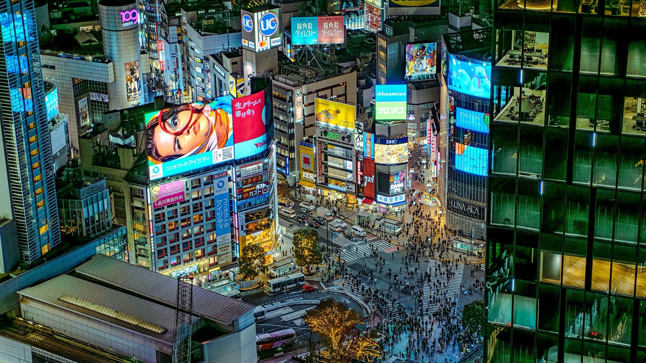 The Shibuya Scramble Crossing at night, seen from above, crowds crossing under neon signage